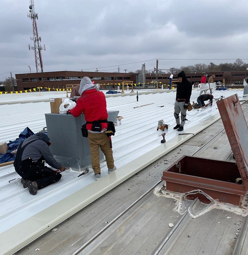 Roofer crew working on top of commercial building to install metal roofing