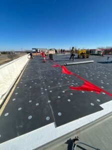 Anchor Roofing team installing black panels and white insulation on a rooftop marked with red safety flags and cones, under clear blue skies in Omaha