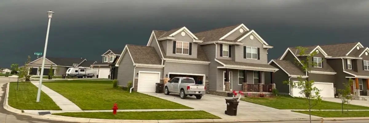 Row of suburban homes with asphalt shingle roofs beneath looming dark storm clouds, illustrating Omaha storm season roof prep storm clouds in Omaha