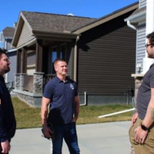 Anchor roofing contractors talking to a roof replacement client in front of a house with black roof and brown siding in Omaha, NE