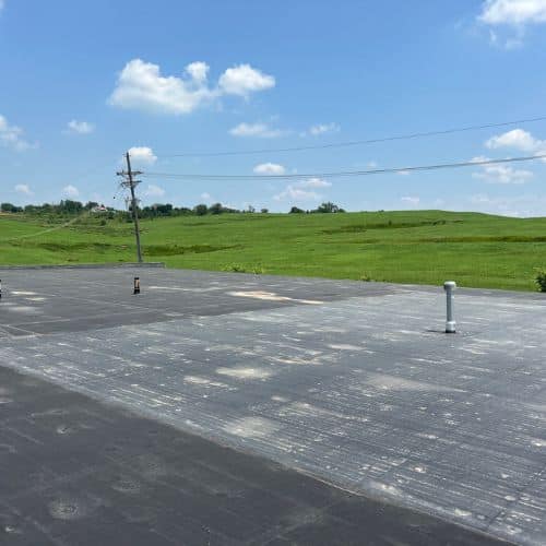 Aerial view of a flat dark roof with vents and pipes with a distance green landscape in Omaha