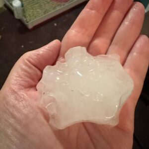 Person holding large, jagged hailstone as a hail size chart example by Anchor Roofing in Omaha, NE