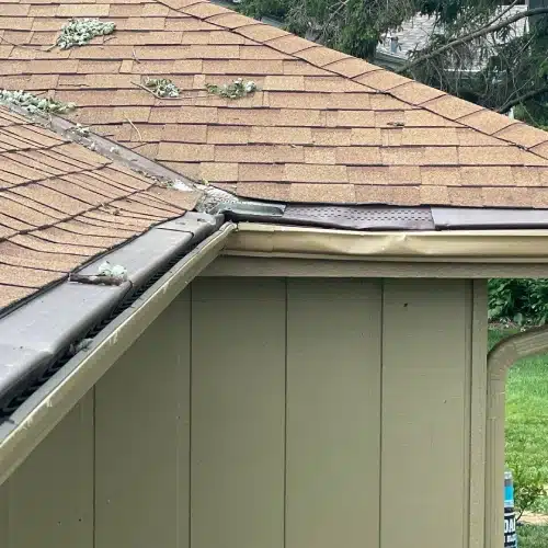 Roof in Gretna, NE with hail damage and debris buildup after a major storm, showing bent gutter and potential shingle impact—Anchor Roofing highlights roofing hail damage Omaha concerns.