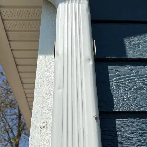 Close-up of hail dents on a white downspout demonstrating how storms cause roof damage by Anchor Roofing in Omaha, NE
