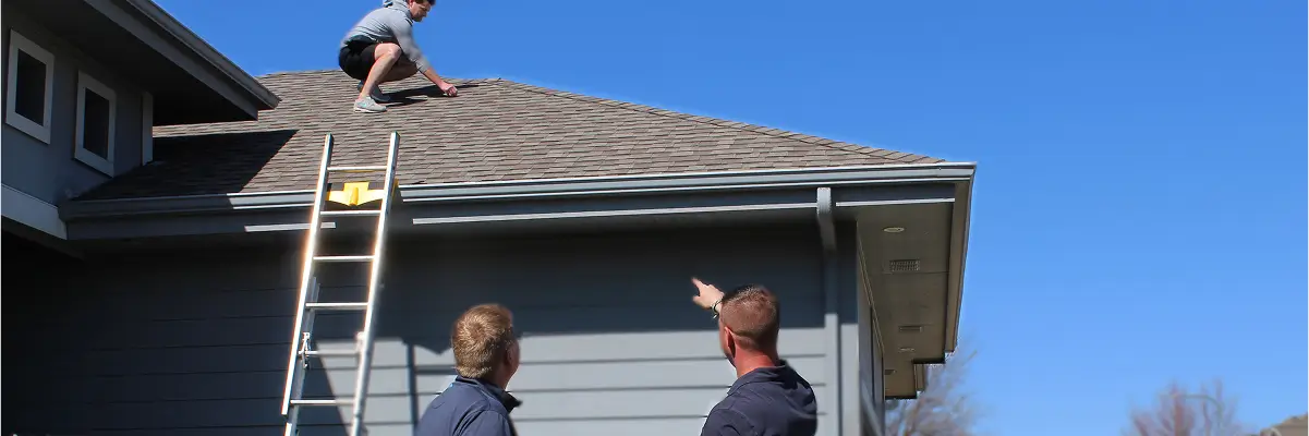 Hand holding hailstones against damaged siding to show impact resistant shingles insurance discount benefits by Anchor Roofing in Omaha, NE