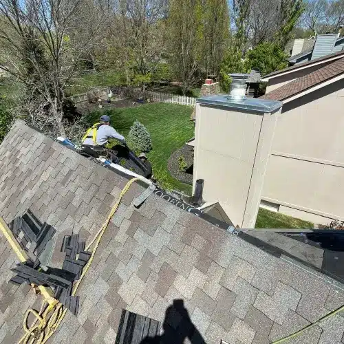 Roofer in safety harness repairing shingle roof valley and installing new materials for roof leak replacement by Anchor Roofing