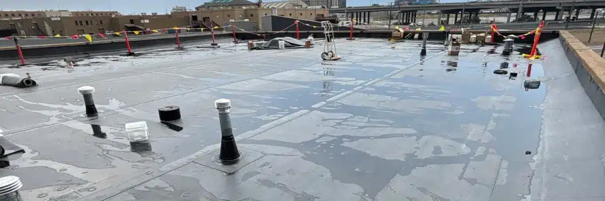 A flat commercial roof with standing water and various vents, awaiting commercial roof replacement by Anchor Roofing.
