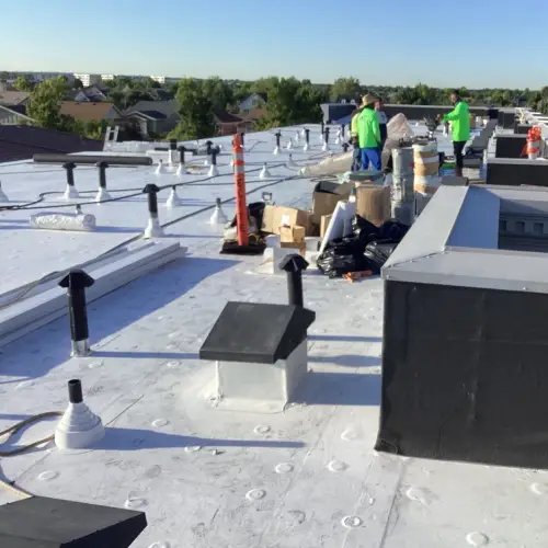 Roofing crew in bright green shirts working on a newly installed white commercial roof, showing vents and equipment for commercial roof replacement by Anchor Roofing.