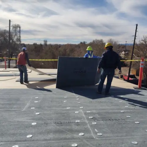 Roofing crew members wearing hard hats and safety gear carefully installing DenSDeck insulation boards during a commercial roof replacement project by Anchor Roofing.