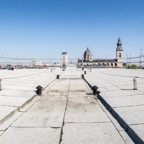 Expansive gray commercial roof surface with vents and a distant city skyline, representing expert commercial roof replacement services by Anchor Roofing.