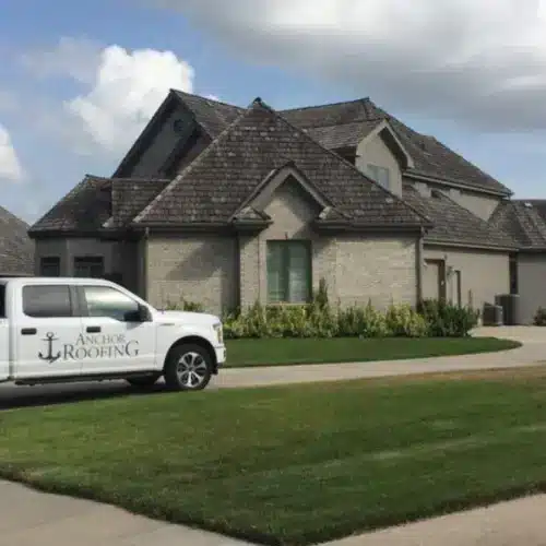 Anchor Roofing service truck parked in front of a residential home during a roof evaluation related to how long is a roof warranty by Anchor Roofing in Omaha, NE