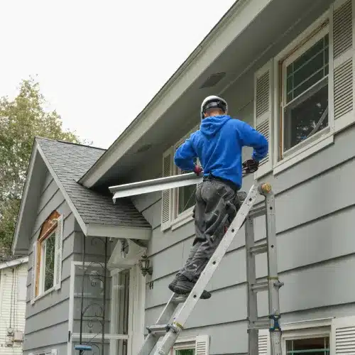 Technician cleaning gutters to winterize siding in Omaha by Anchor Roofing | Omaha's Best Roofing Contractor