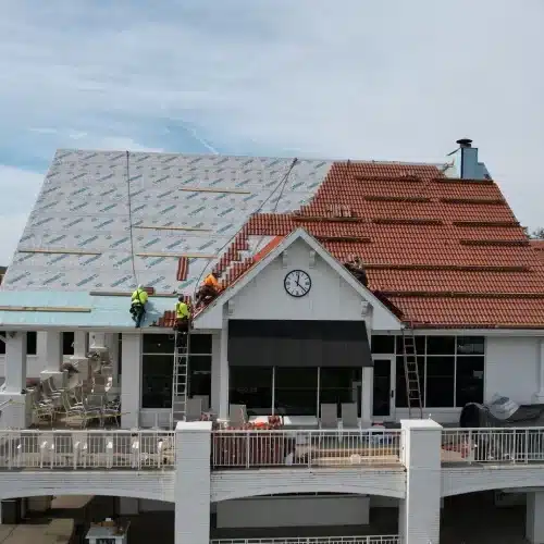 Roofers setting Brava synthetic Spanish tiles beside underlayment on the steep clubhouse roof with central clock at Happy Hollow—iconic Omaha roof replacement by Anchor Roofing in Omaha