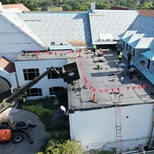 Crew installing Carlisle EPDM on a flat roof with crane support at Happy Hollow Country Club during an iconic Omaha roof replacement by Anchor Roofing in Omaha