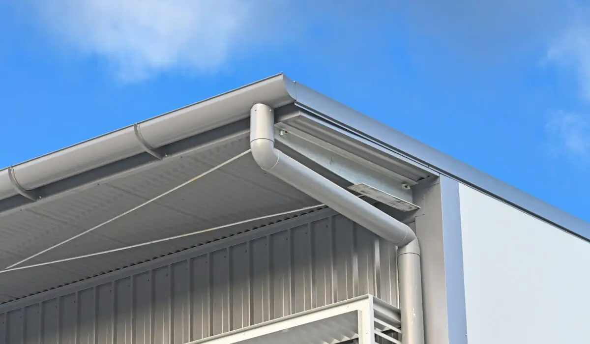 Close-up of a modern commercial metal gutter and downspout under blue sky, highlighting durable gutters in Omaha by Anchor Roofing in Omaha
