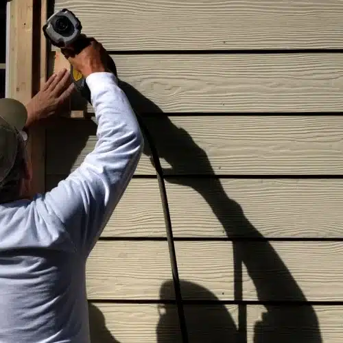 Siding contractor securing fiber cement lap siding with a nail gun by Anchor Roofing in Omaha