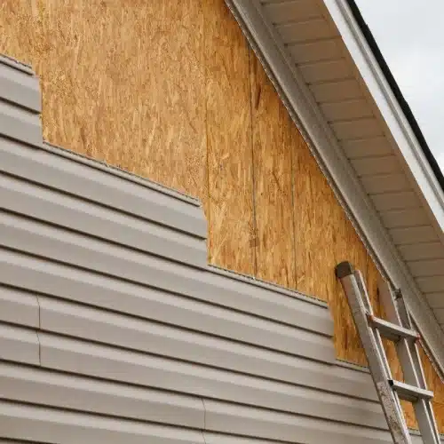 Siding contractor work showing new vinyl siding next to exposed sheathing and ladder by Anchor Roofing in Omaha