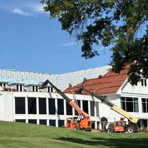 Two telehandlers hoist roofing materials as crews install Brava tiles on the clubhouse roof at Happy Hollow Country Club—iconic Omaha roof replacement by Anchor Roofing in Omaha