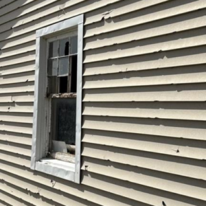 Close-up of damaged and warped siding panels on a house exterior showing wear before replacement