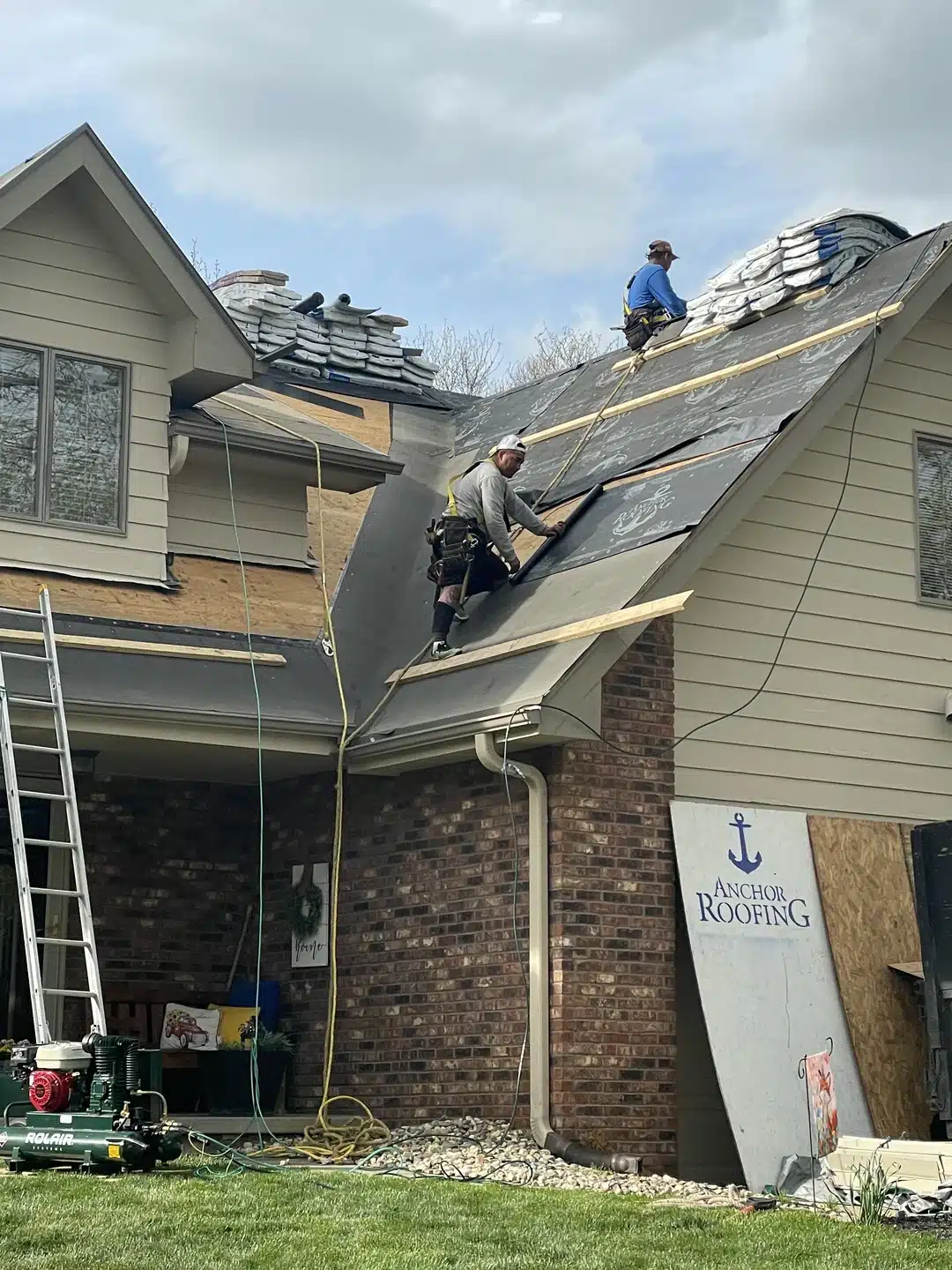 Roofers from Anchor Roofing installing new roofing materials on a residential home in Omaha, working on a steep roof with safety gear and equipment visible.