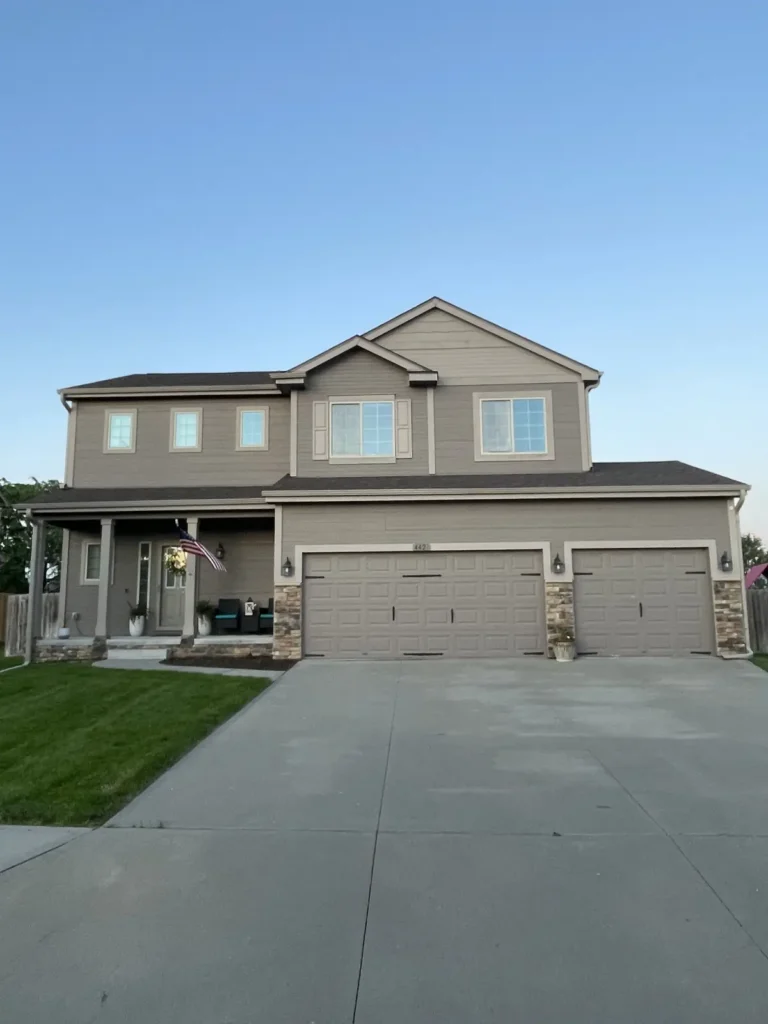 A two-story Omaha home with a dark shingle roof, three-car garage, and well-kept exterior, showcasing a completed roofing project by Anchor Roofing.