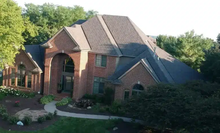 Aerial view of a large brick home in Omaha featuring a dark asphalt shingle roof, showcasing a completed residential roofing project by Anchor Roofing.