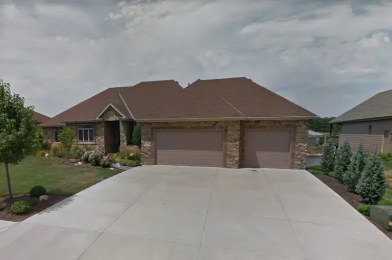 Front view of an Omaha home with a brown asphalt shingle roof, stone exterior accents, and a wide driveway, showcasing a completed residential roofing project by Anchor Roofing.