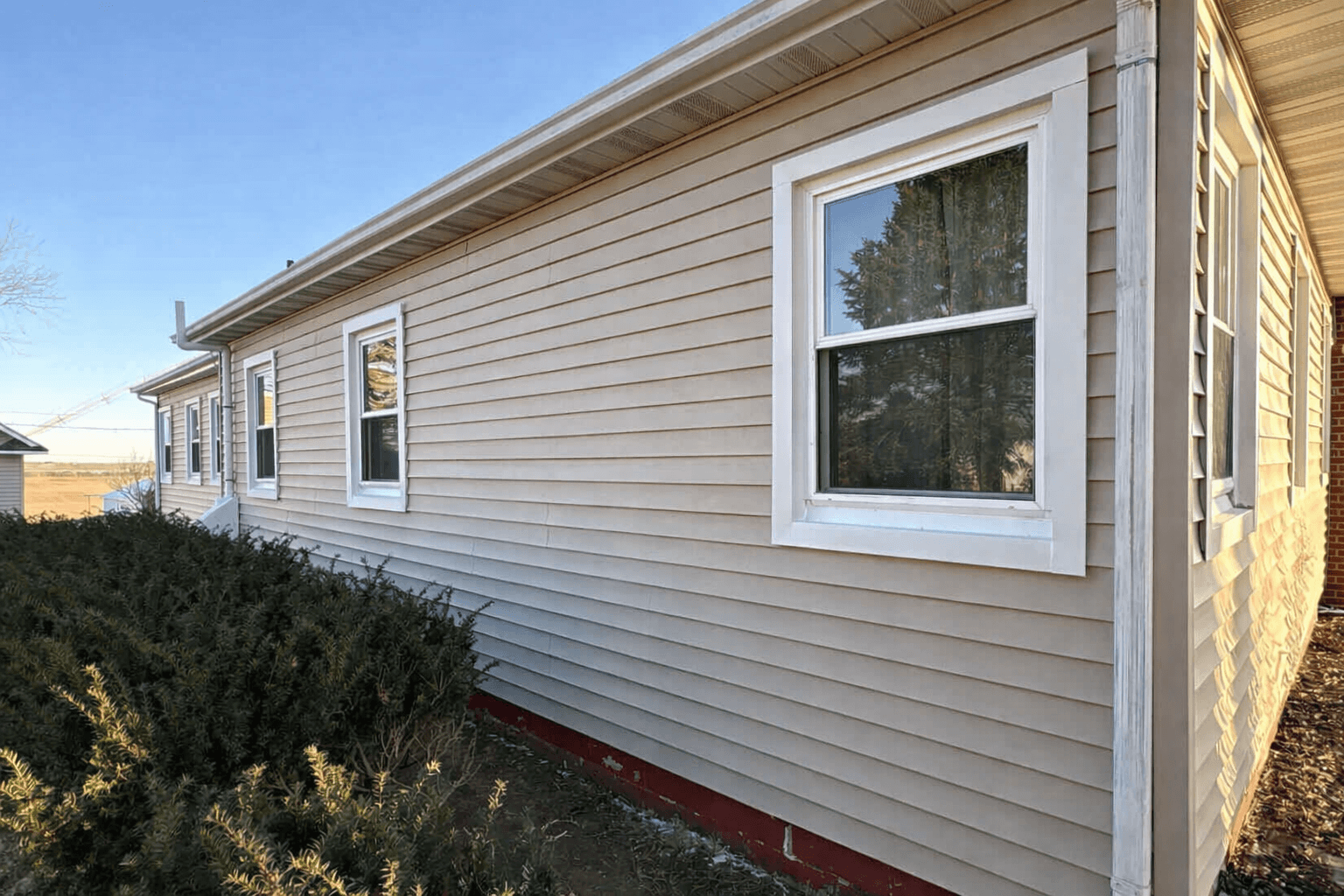 Beige siding house with shrubs featuring siding energy efficiency service in Omaha, NE by Anchor Roofing