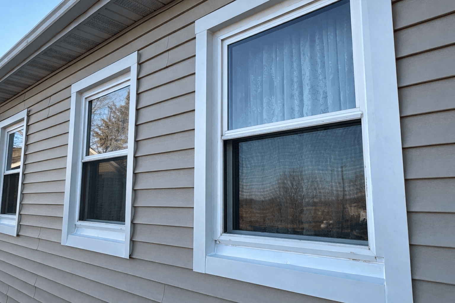 Beige vinyl siding wall with three windows showcasing siding energy efficiency service in Omaha, NE by Anchor Roofing