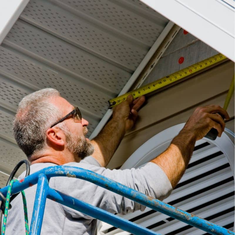 A siding installer measuring exterior soffit and trim details for a top-rated siding installer in Omaha by Anchor Roofing.