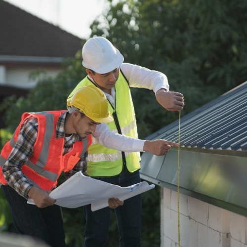 Two construction contractors measuring a metal roofline with a tape measure to review roof insurance check rules residential roof inspection in Omaha by Anchor Roofing