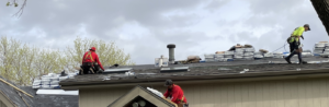 A roofing crew tearing off old shingles and prepping a multi-level roof with materials that act as roof replacement pricing factors residential roof replacement in Omaha by Anchor Roofing