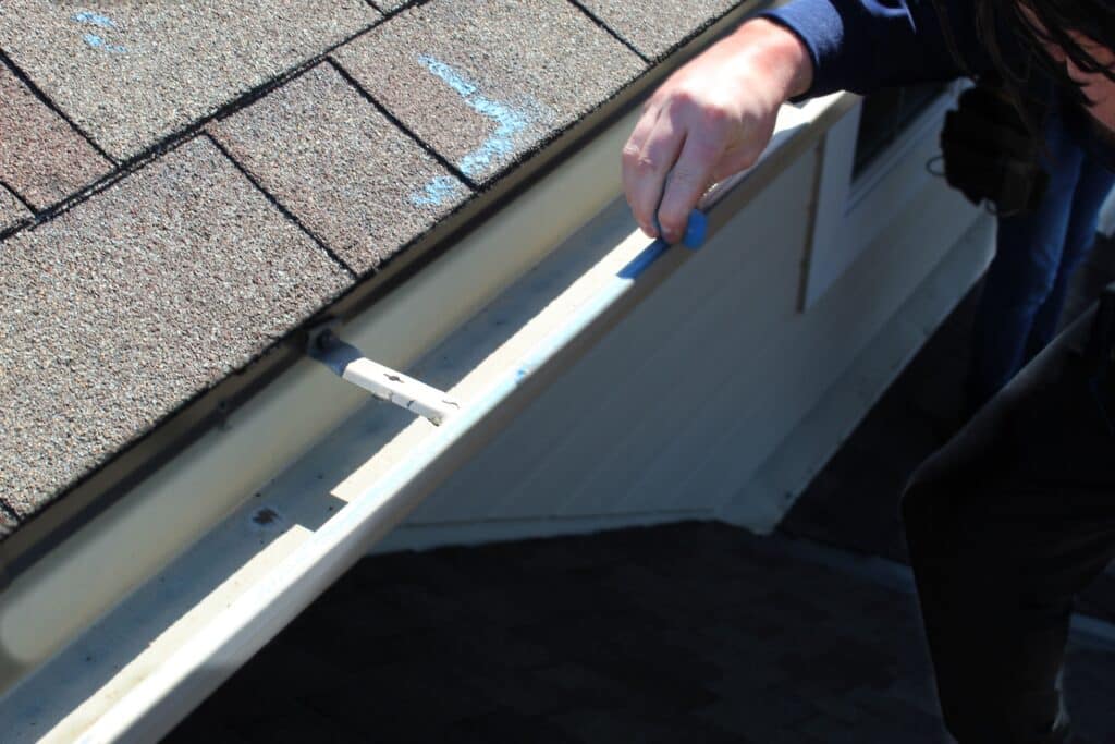 A technician marking storm damage on a metal gutter with blue chalk during commercial roof maintenance commercial roof inspection in Omaha by Anchor Roofing