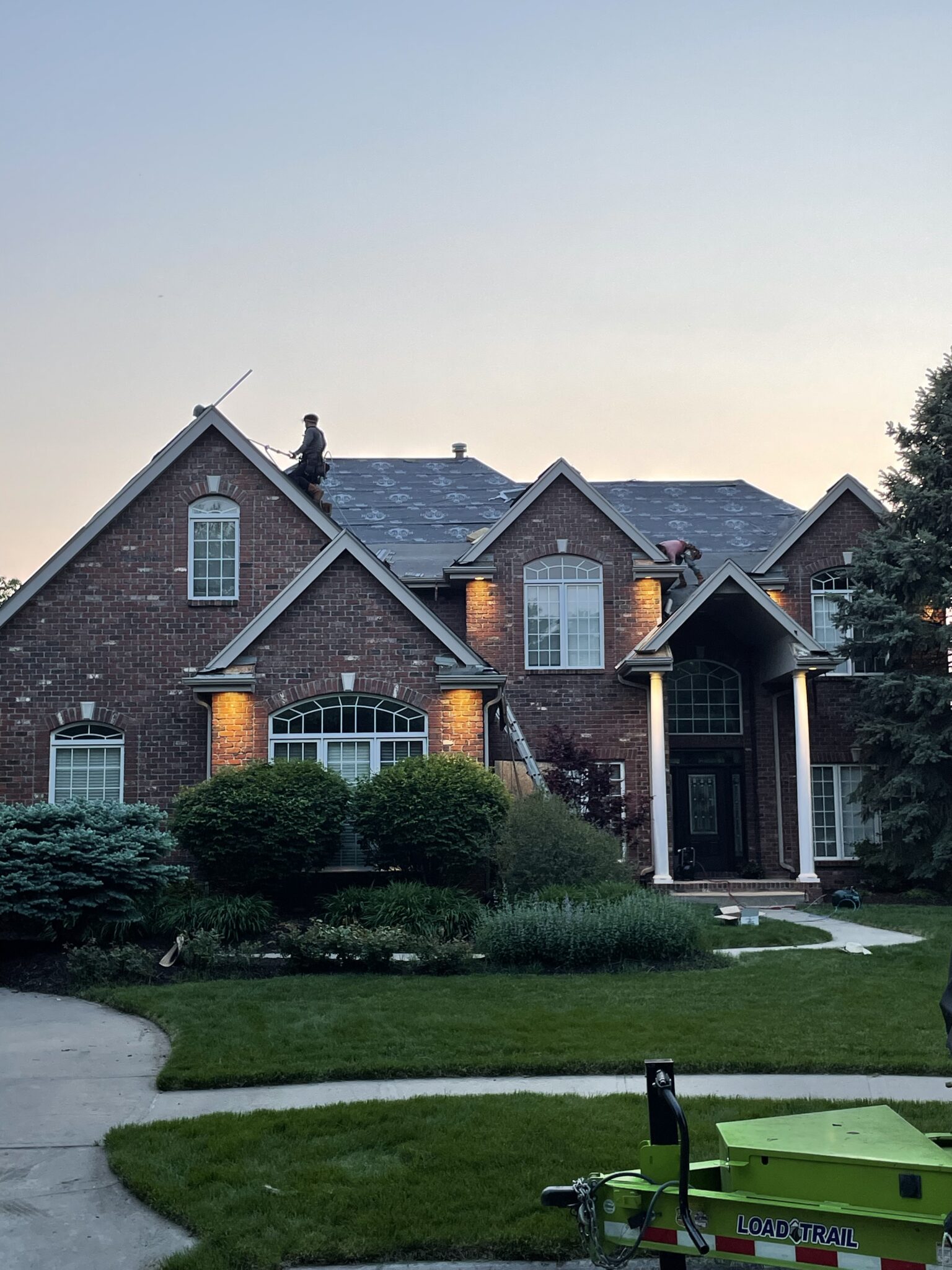 Workers installing underlayment on a steep brick home's roof to comply with roof insurance check rules residential roof replacement in Omaha by Anchor Roofing