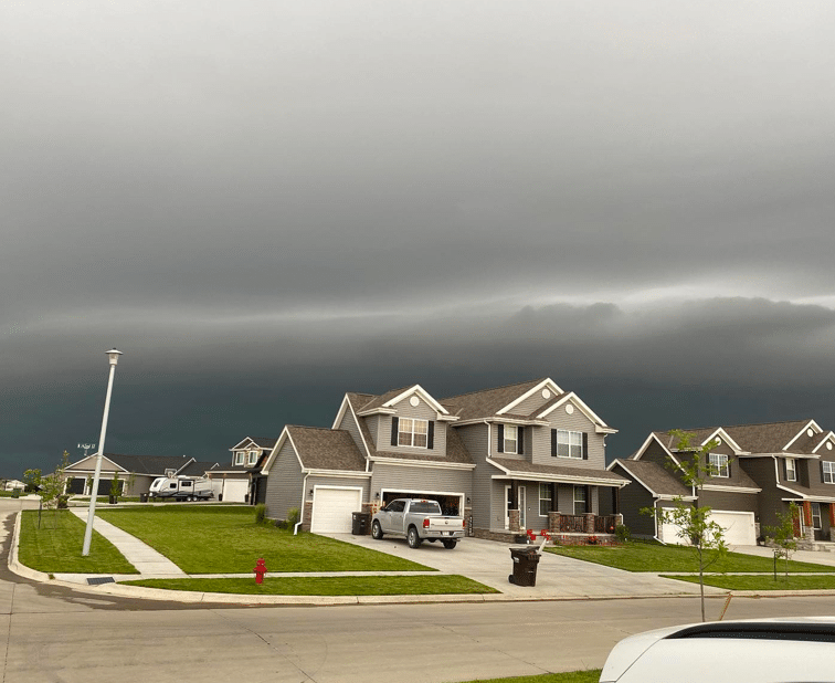 Storm clouds loom over a residential neighborhood showcasing complex asphalt shingle architecture that impacts roof replacement pricing factors storm damage inspection in Omaha by Anchor Roofing