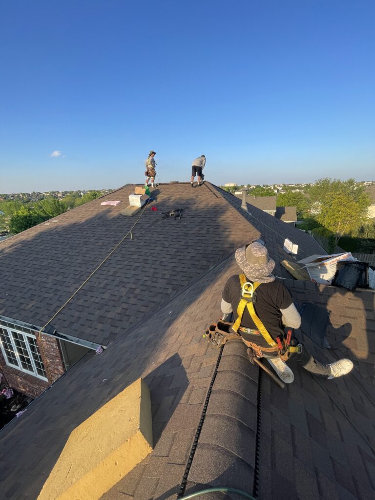 Roofing crew working on a steep shingle roof ridge near staged materials following asphalt shingle storage residential roof replacement in Omaha by Anchor Roofing