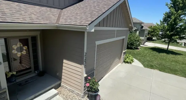 Front view of a well-maintained Omaha home with a newly installed shingle roof, clean siding, and a neat driveway under a clear blue sky.